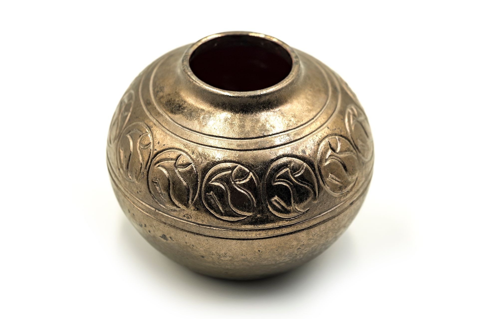 Antique bronze pot with intricate carvings and a round opening, isolated on a white background.